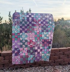 a very large patchwork quilt sitting on top of a brick wall next to some trees