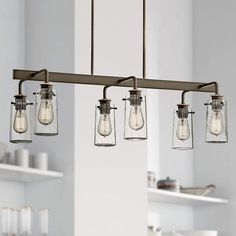 three mason jar lights hanging from a kitchen light fixture over a counter top with utensils on it