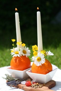 two oranges with daisies and flowers in them on a tablecloth next to some candles