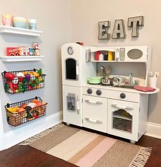 a play kitchen with white cabinets and wooden floors