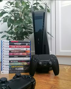 a stack of video games sitting on top of a wooden table next to a plant