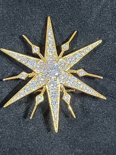 a gold and diamond star brooch on a black surface with white diamonds in the center