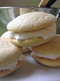 three biscuits with cream fillings are stacked on a plate in front of a silver bowl