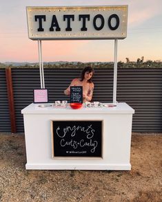 a woman standing behind a white counter with a sign on it that says, tattoo