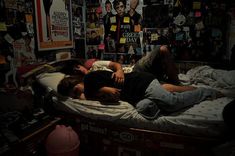 two people laying on a bed in a room with many pictures and posters all over the wall