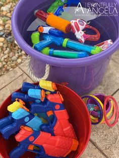 a bucket filled with lots of toys on top of a stone floor next to a purple pail