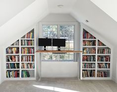 a room with bookshelves and a computer monitor on the desk in front of two windows