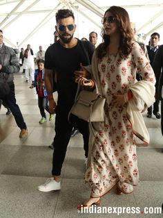 a man and woman walking through an airport with people in the background, all wearing sunglasses