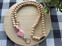 a wooden beaded necklace with a pink heart charm on a wood plate next to a potted plant