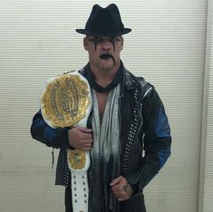 a man wearing a hat and scarf holding a wrestling belt