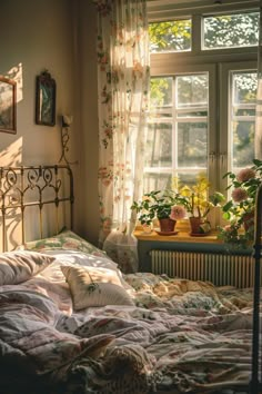 an unmade bed in front of a window with potted plants