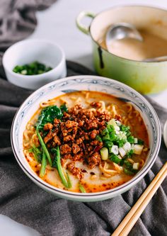 a bowl filled with noodles, meat and vegetables on top of a table next to chopsticks