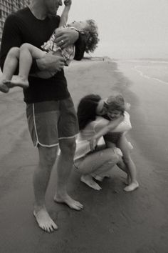 a man holding a baby while standing next to two other people on the beach,