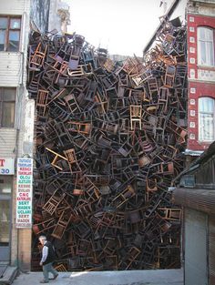 a large pile of chairs sitting on the side of a building next to a man