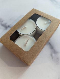 three white candles in a cardboard box on a marble countertop with the lid open