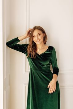 a woman in a green dress leaning against a wall with her hands on her head