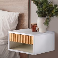 a white nightstand with a plant and candle on it next to a bed in a bedroom