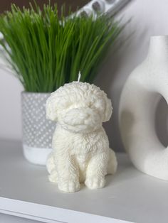 a small white dog figurine sitting on top of a shelf next to a plant