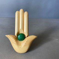 a wooden sculpture with a green ball in the middle of it's palm, sitting on a gray surface