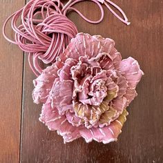 a pink flower sitting on top of a wooden table next to a string and cord