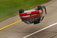 a red truck is flying through the air on a road with grass in the background