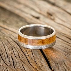 a wooden ring with silver and wood inlays sits on a piece of wood