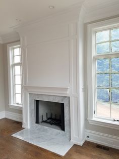 an empty living room with a fireplace and two windows in the corner, all painted white