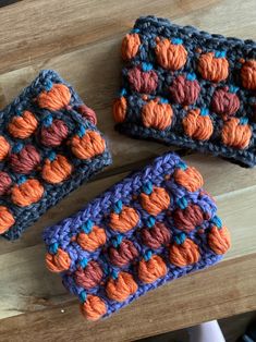 three crocheted squares sitting on top of a wooden table next to each other