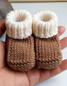 a hand is holding two baby booties in brown and white knitted yarns