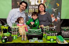 two adults and one child are standing in front of a table with green decorations for st patrick's day