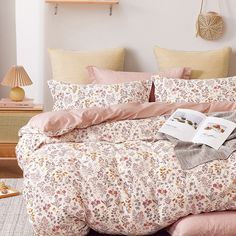 a bed with pink comforter and pillows in a white room next to a lamp