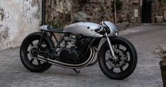 a silver motorcycle parked on top of a brick road next to a wall and planters