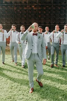 a group of men in suits and bow ties are walking through the grass with beer