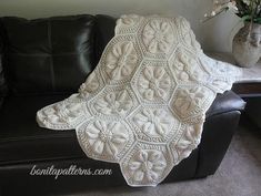 a white crocheted blanket sitting on top of a black couch next to a vase with flowers