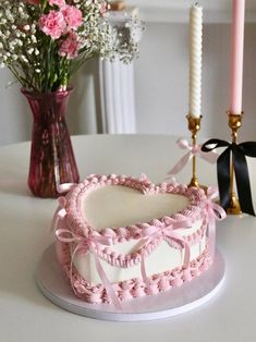 a pink heart shaped cake sitting on top of a table next to a vase with flowers