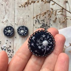 a person holding a dandelion brooch in their left hand next to other items