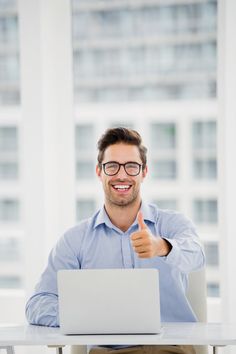 a man sitting at a table with a laptop giving a thumbs up