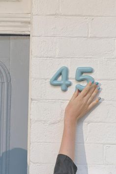 a woman's hand reaching up to the number 45 on a white brick wall