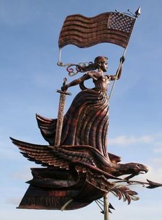 a statue of a woman holding an american flag on top of a bird shaped pole