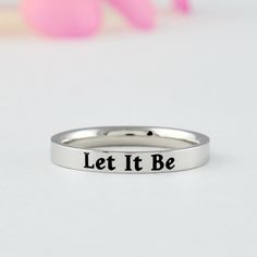 "This listing is for one stainless steel band ring, engraved with \"Let It Be\" on the outside. It makes an inspirational and motivational gift for best friends or just yourself. Materials & Features: This ring is made of high quality hand polished solid stainless steel, which is hypoallergenic (good for metal-sensitive skin). Stainless steel will not tarnish, its luster and durability will make it last for many years. The black text on the ring will not fade out over time. Sizes: This ring is 3 Elevated Faith Rings, Cute Rings Elevated Faith, Silver Stackable Spiritual Rings, Adjustable Stainless Steel Engraved Ring, Spiritual Engraved Metal Rings, Silver Music-themed Rings For Gifts, Encouragement Gift, Friend Bff, Sorority Sisters