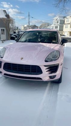 a pink porsche parked in the snow on a residential street with houses and cars behind it