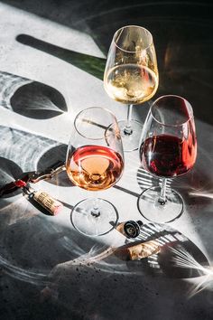 two glasses of wine sitting next to each other on top of a table with bottles and corks