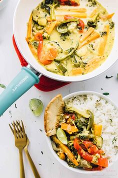 two bowls filled with vegetables and rice on top of a white table next to silverware