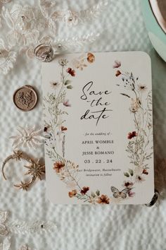 wedding save the date cards and rings on a white lace tablecloth with flowers, leaves and coins