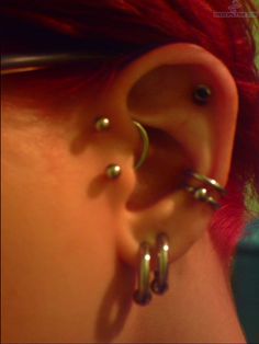 a woman with red hair has three piercings on her ear and one behind the ear