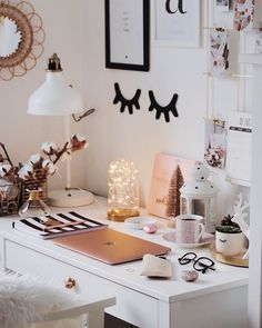 a white desk topped with a laptop computer next to a lamp and pictures on the wall