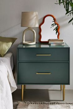 a nightstand with a mirror on it next to a bed and a plant in the corner