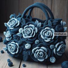 a blue purse with flowers on it sitting on a wooden table next to balls of yarn