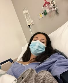 a woman laying in a hospital bed wearing a face mask