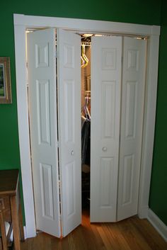 two white doors open in a room with green walls and hardwood floors, along with a wooden table